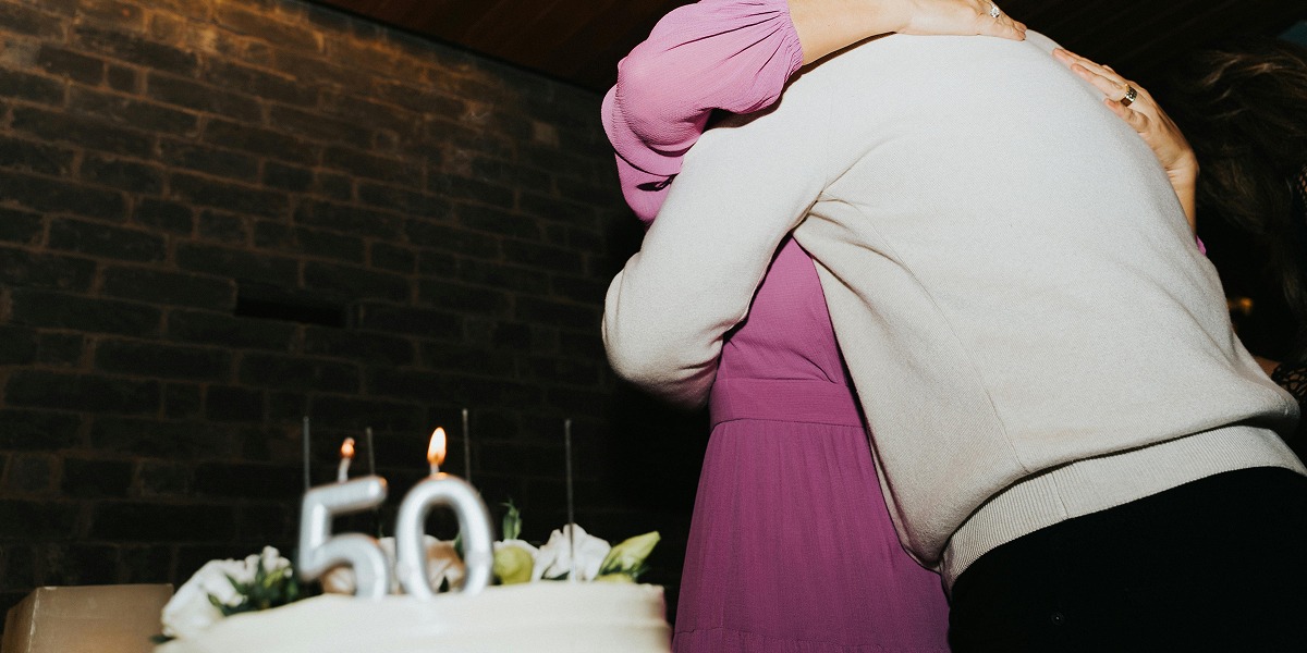 Dos personas abrazadas con un pastel detrás