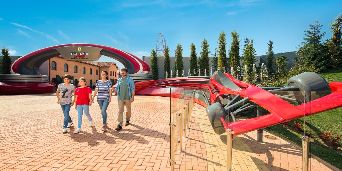 Familia paseando por la entrada de Ferrari Land con un monoplaza Ferrari expuesto durante el GP Festival