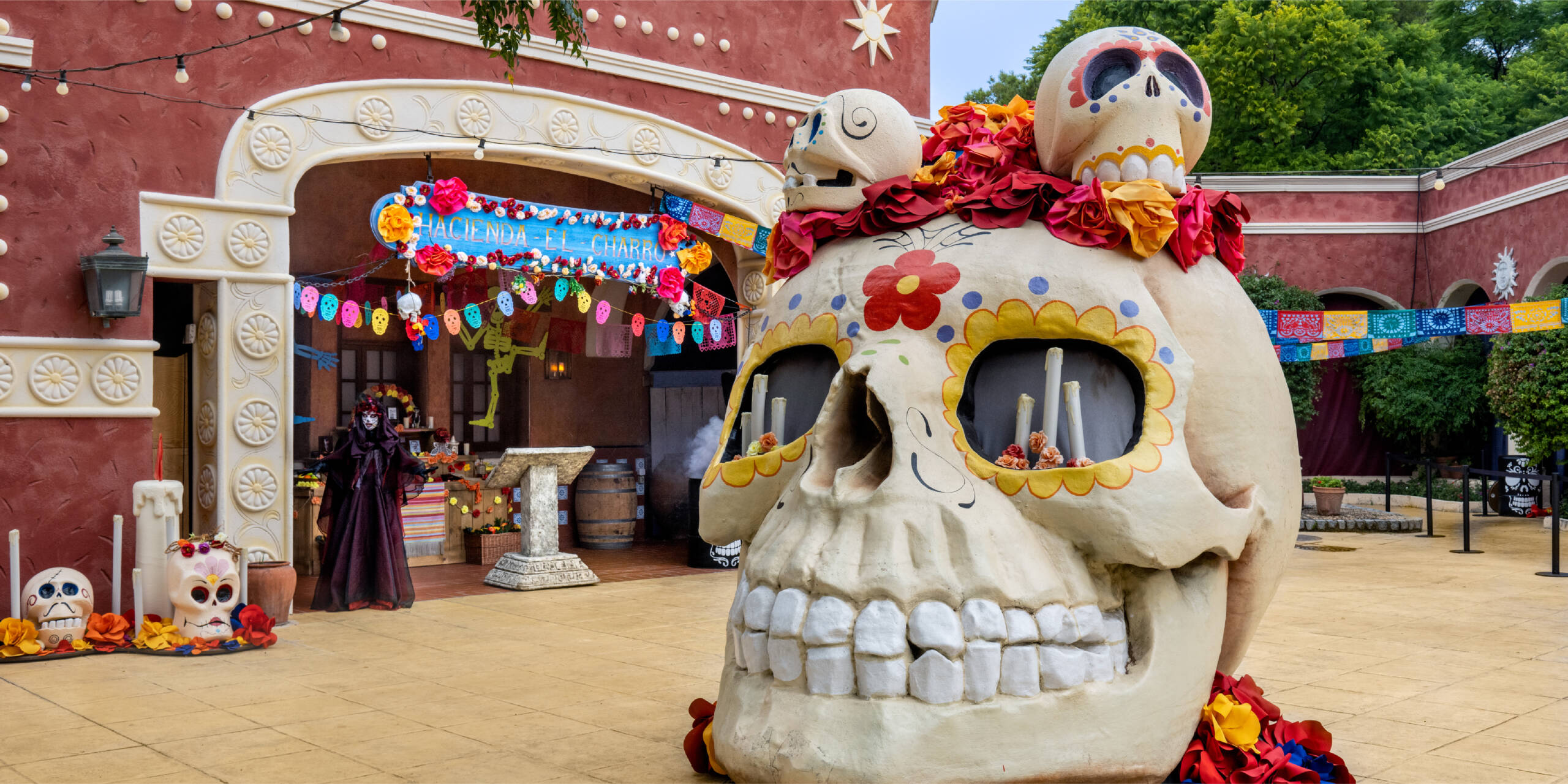 Gran calavera decorada con flores de colores y banderines festivos en una plaza ambientada para Halloween