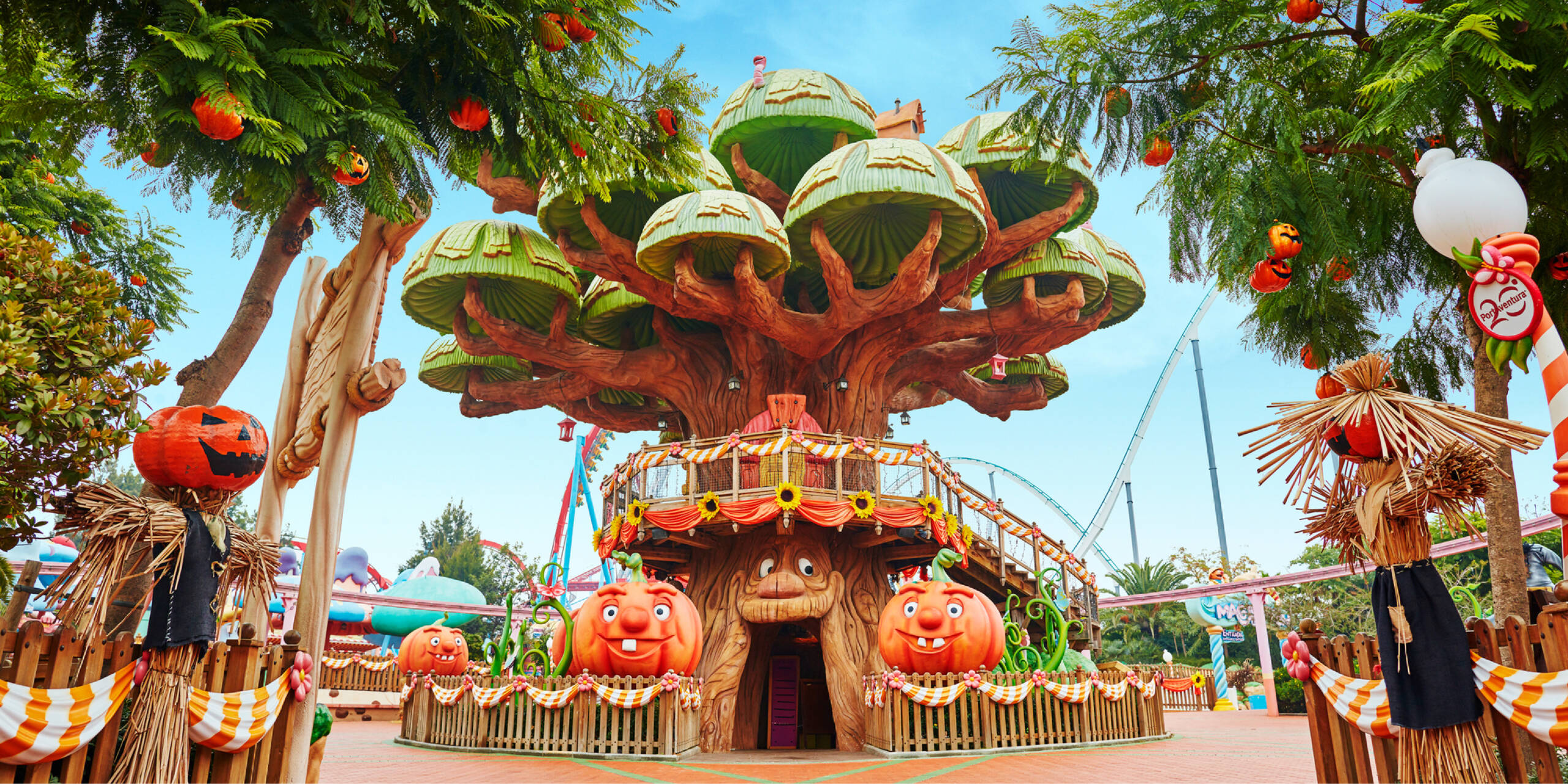 Casa del árbol decorada con calabazas gigantes y espantapájaros para Halloween, con montañas rusas al fondo