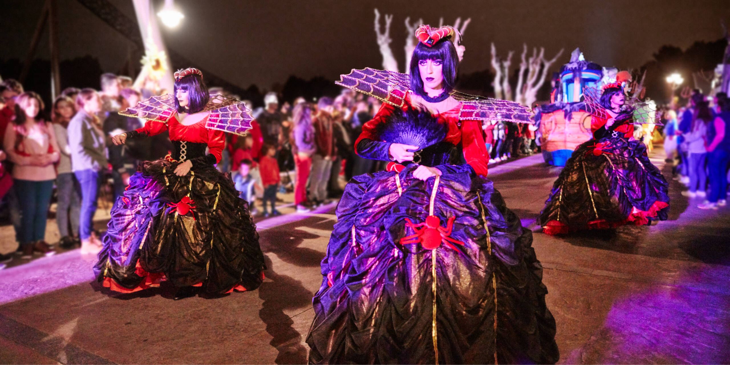 Artistas con trajes oscuros y rojos desfilando de noche ante el público en la Halloween Parade de PortAventura Park